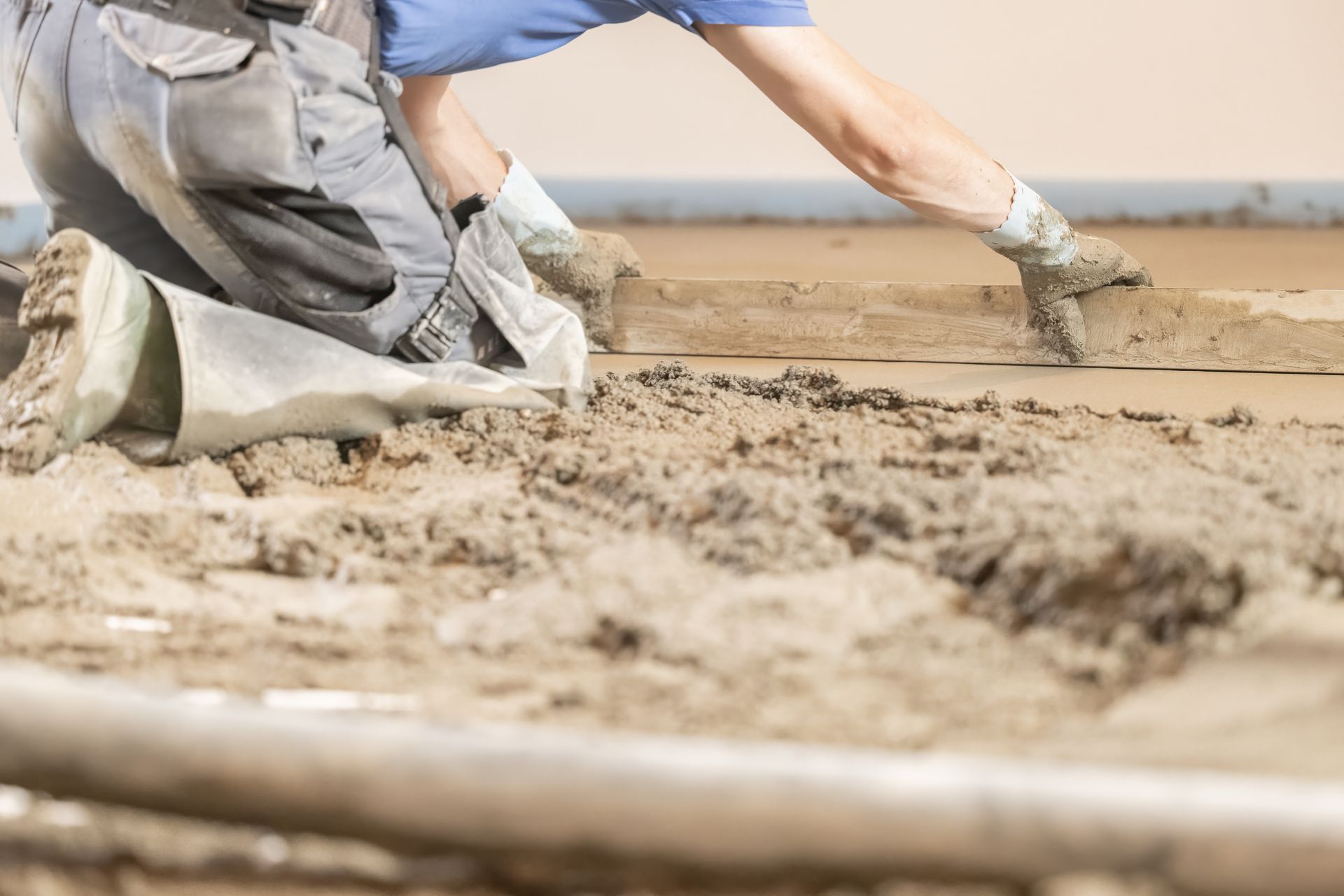 Ouvrier du bâtiment à genoux, lissant le béton humide avec une chape dans un environnement intérieur.