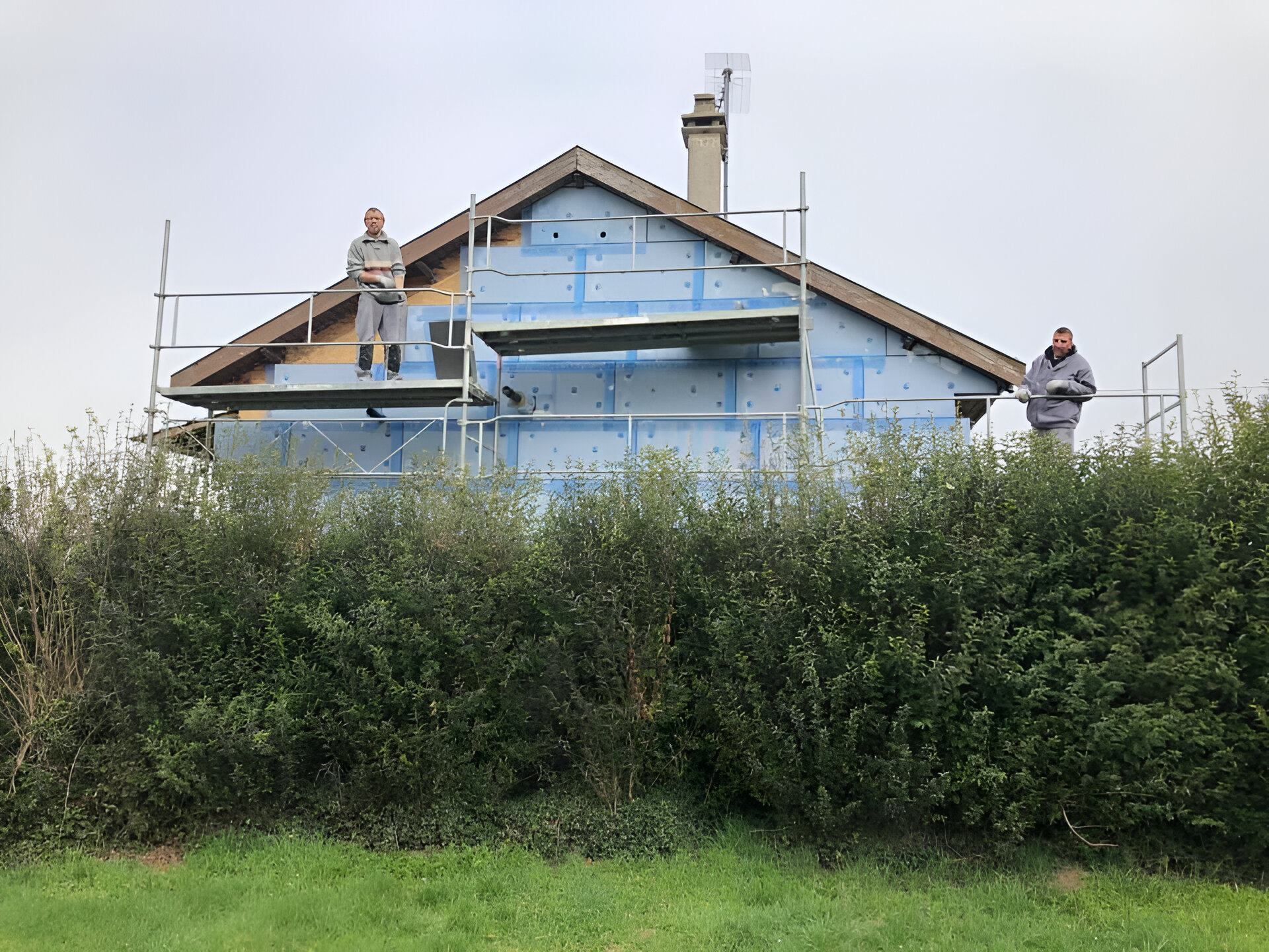 Deux personnes sur un échafaudage installent une isolation bleue sur une maison en construction. 