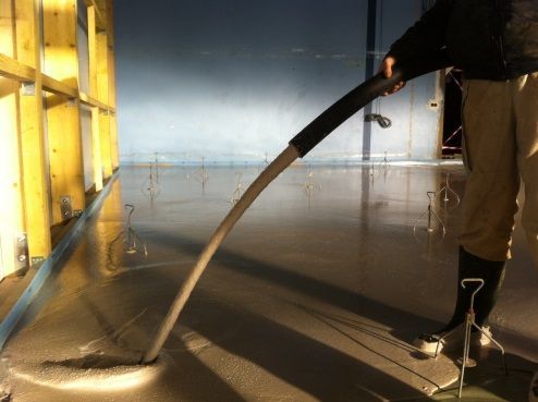 Un ouvrier coule une chape liquide à l'intérieur d'un bâtiment en construction.
