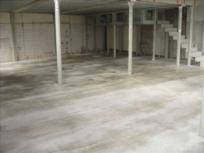 Sous-sol non aménagé, sol en béton. Des colonnes soutiennent une partie surélevée avec escalier. Murs en béton carrelés.