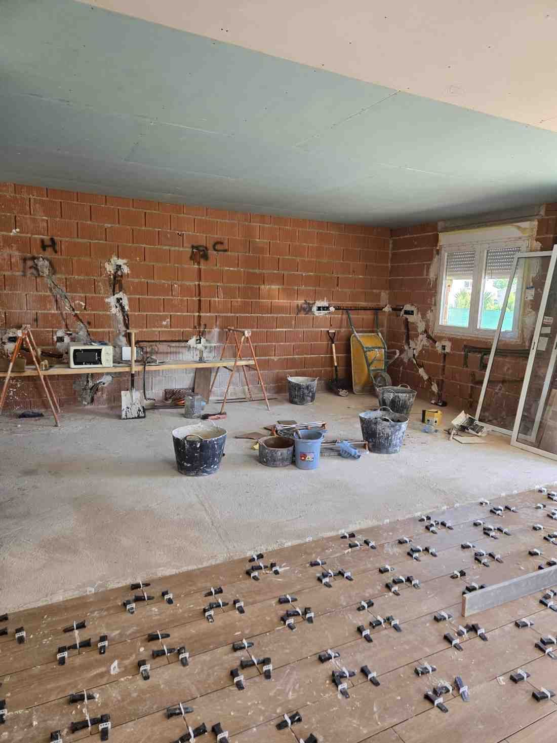 Habitación sin terminar con paredes de ladrillo, herramientas, cubos y materiales de trabajo esparcidos por el suelo.