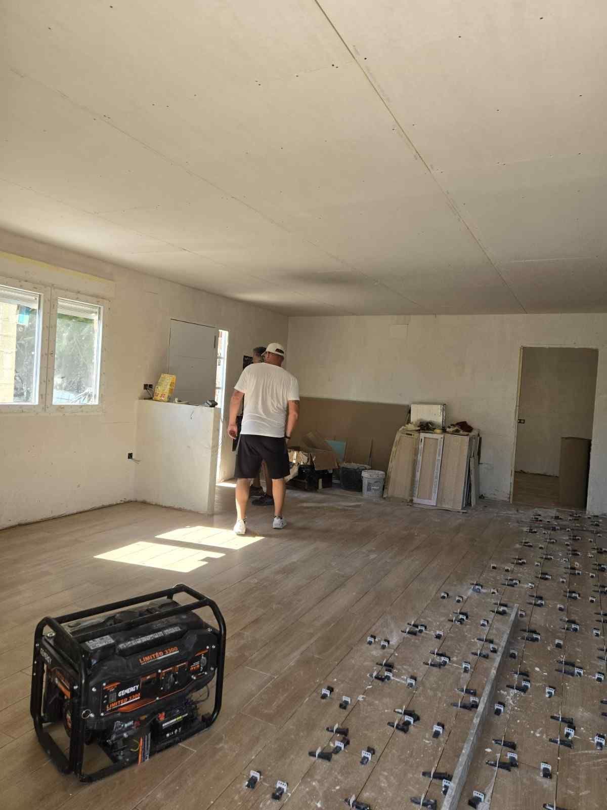 Un trabajador se encuentra en una habitación vacía e iluminada por el sol, instalando pisos con herramientas.