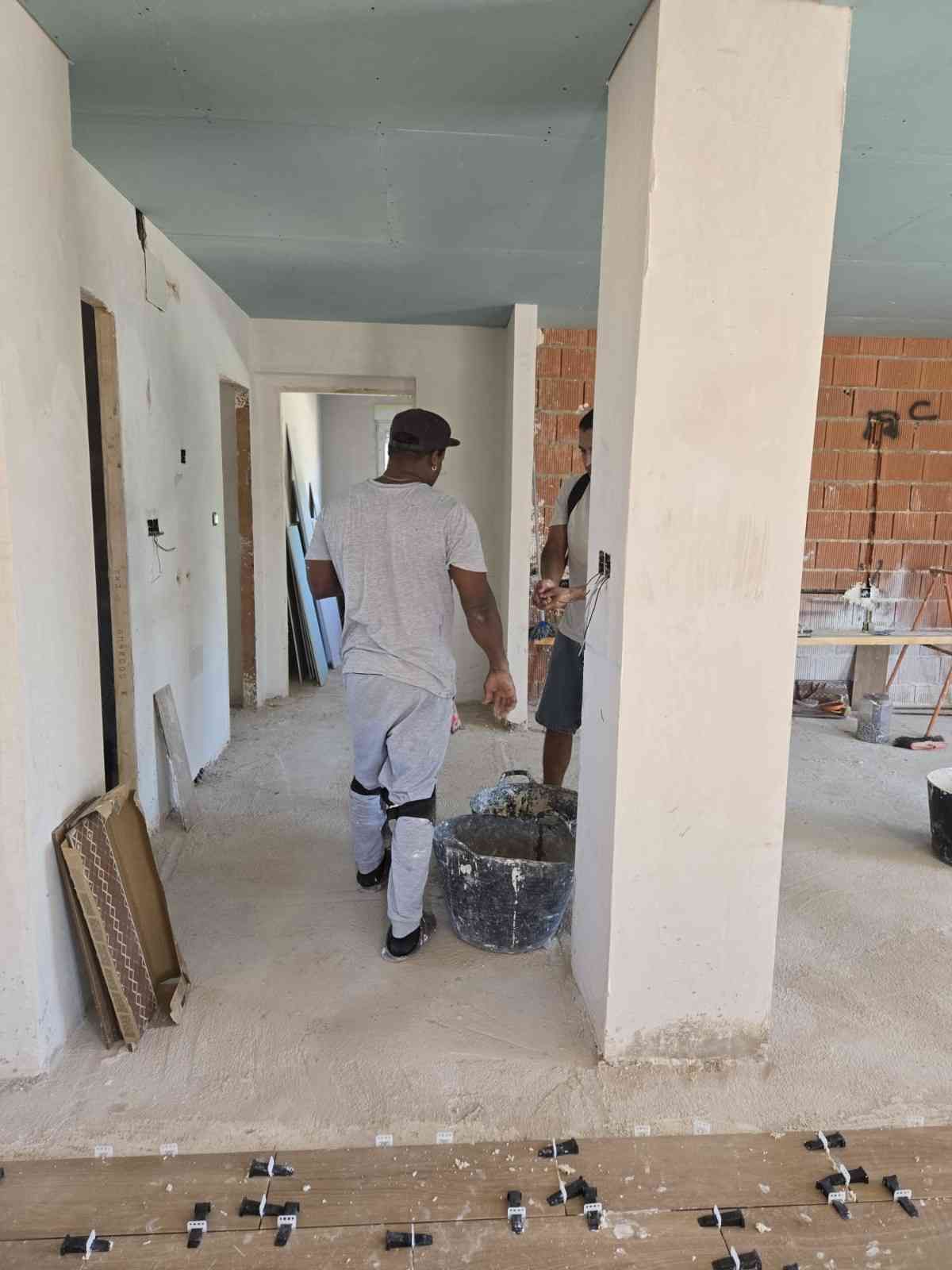 Dos trabajadores caminan por un pasillo sin terminar con paredes blancas y ladrillo visto.