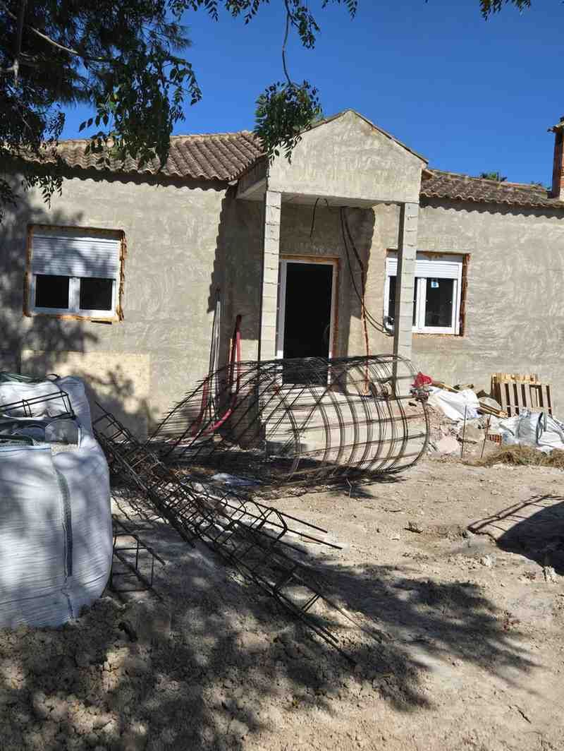 Casa parcialmente construida con paredes de estuco, puerta de entrada, materiales de construcción.