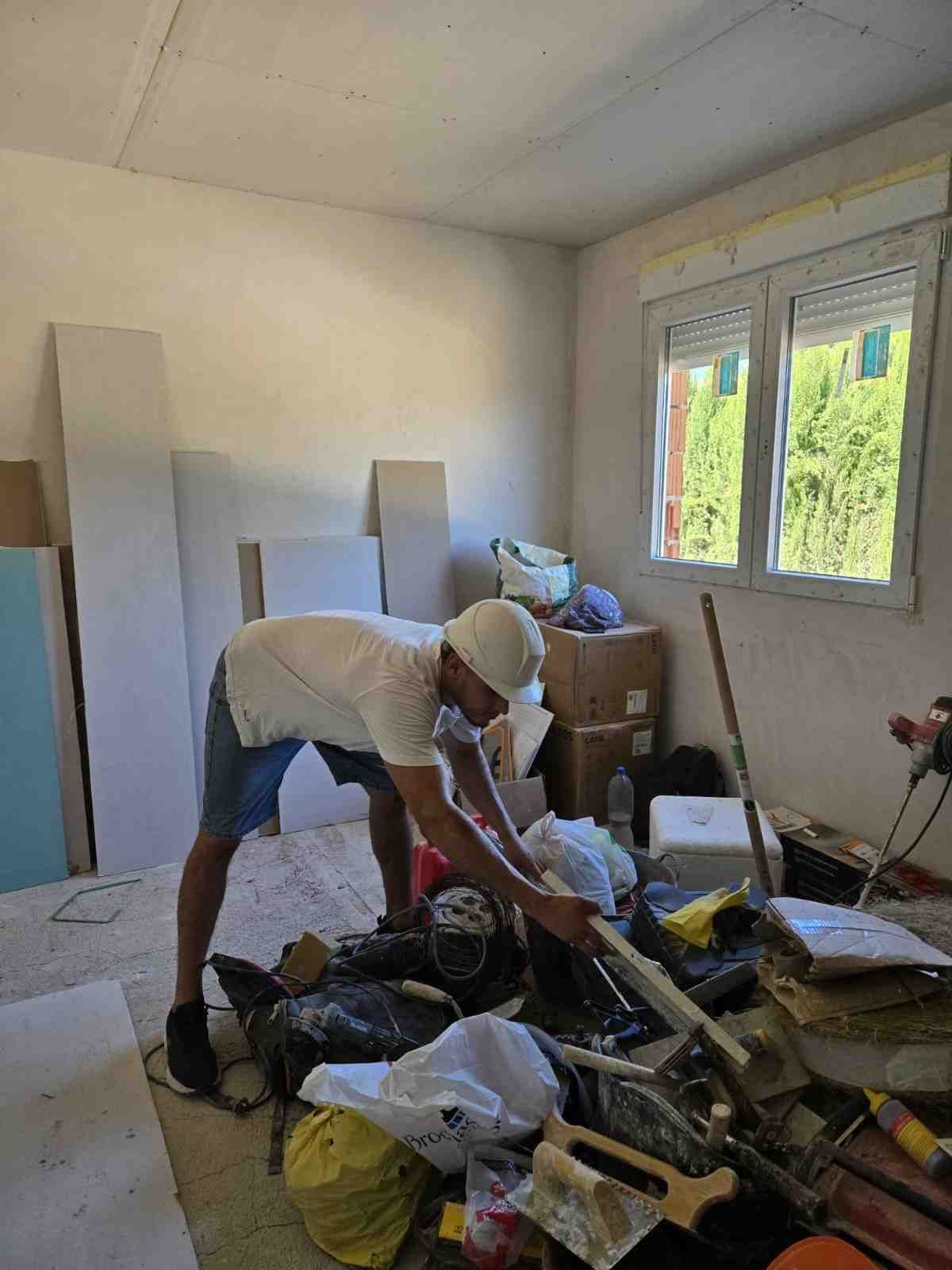 Una persona está revolviendo una pila de objetos desechados en una habitación desordenada cerca de una ventana.