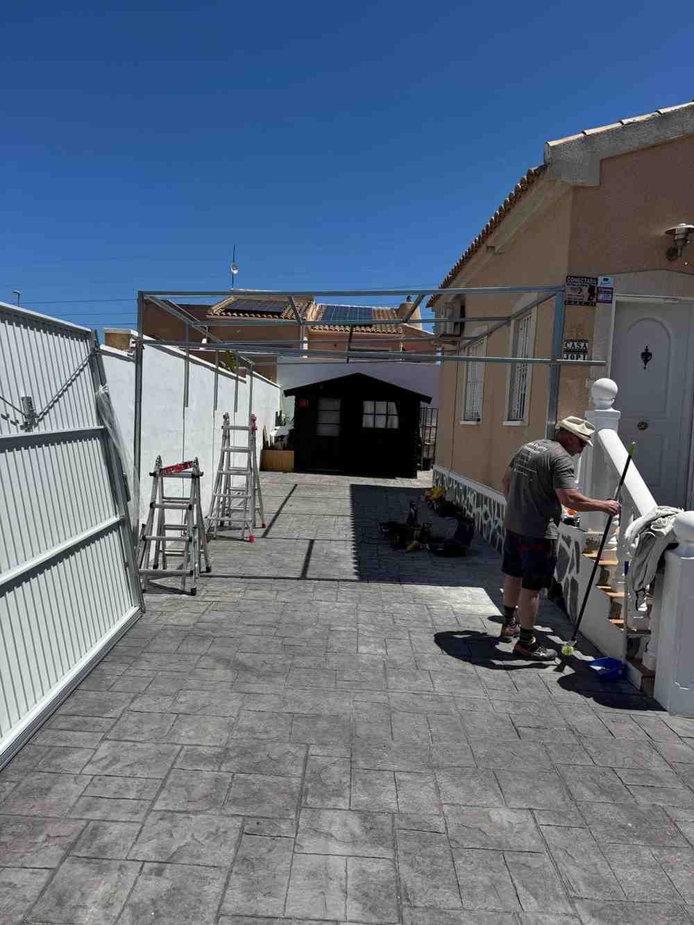 Sendero trasero con adoquines de piedra recién instalados y trabajadores cerca de una casa en un día soleado.