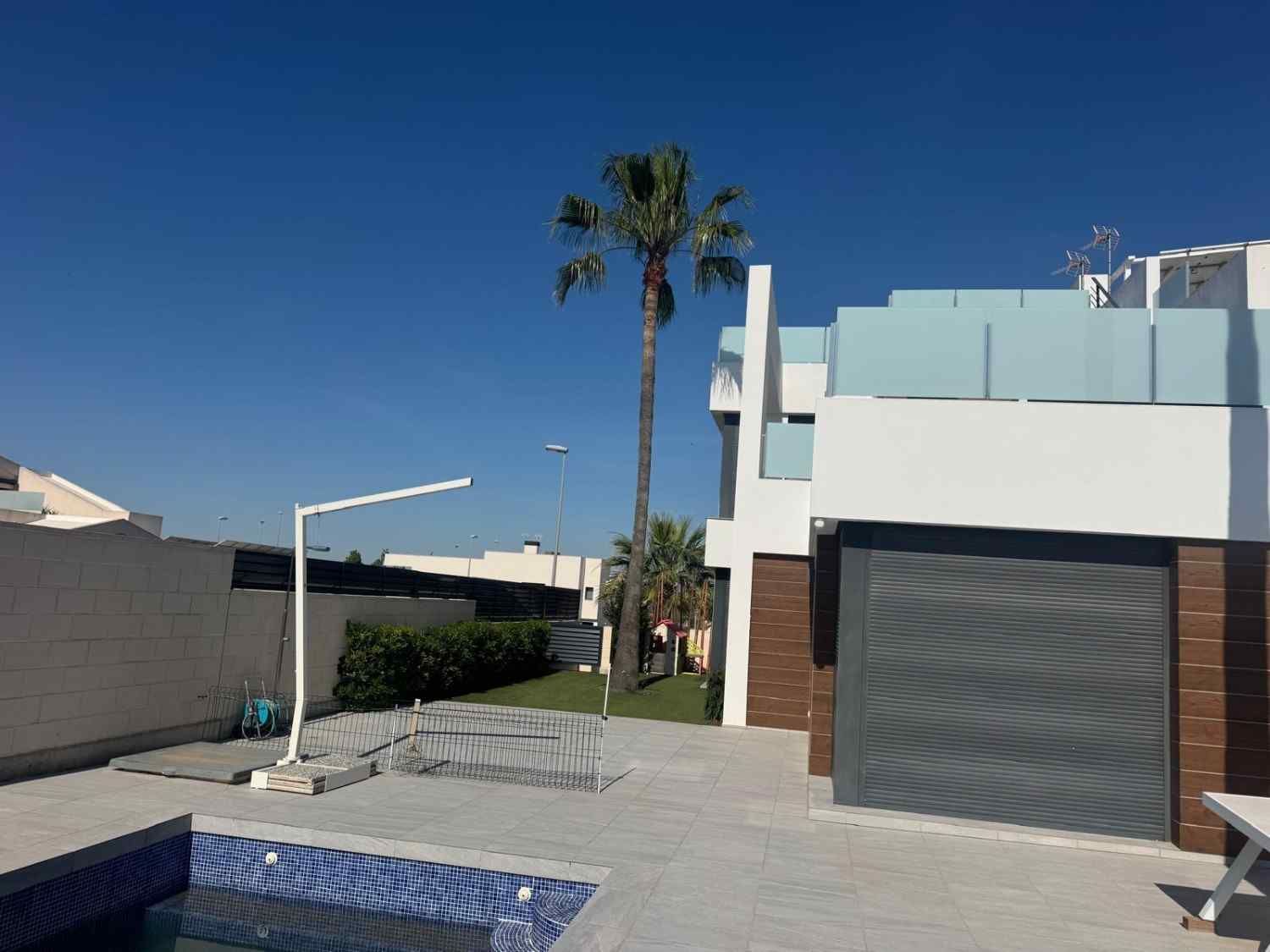 Casa moderna con garaje, piscina, palmeras y cielo azul despejado.