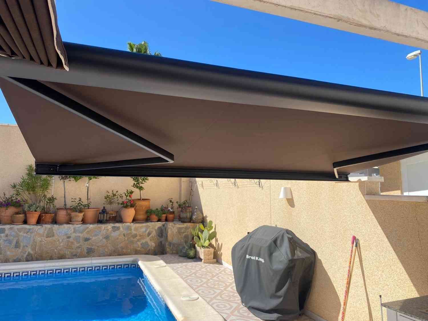 Patio con toldo retráctil sobre una piscina y parrilla cubierta en el patio trasero.