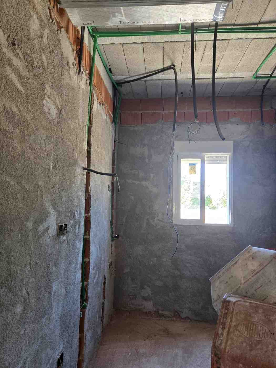 Habitación sin terminar con paredes de yeso rugoso, cables expuestos en el techo y una pequeña ventana.