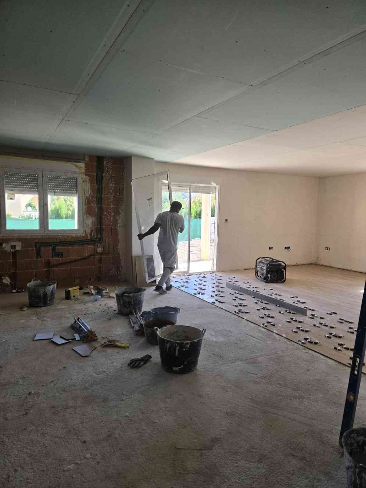 Un trabajador pinta una habitación en obras, con herramientas y cubos esparcidos por el suelo.