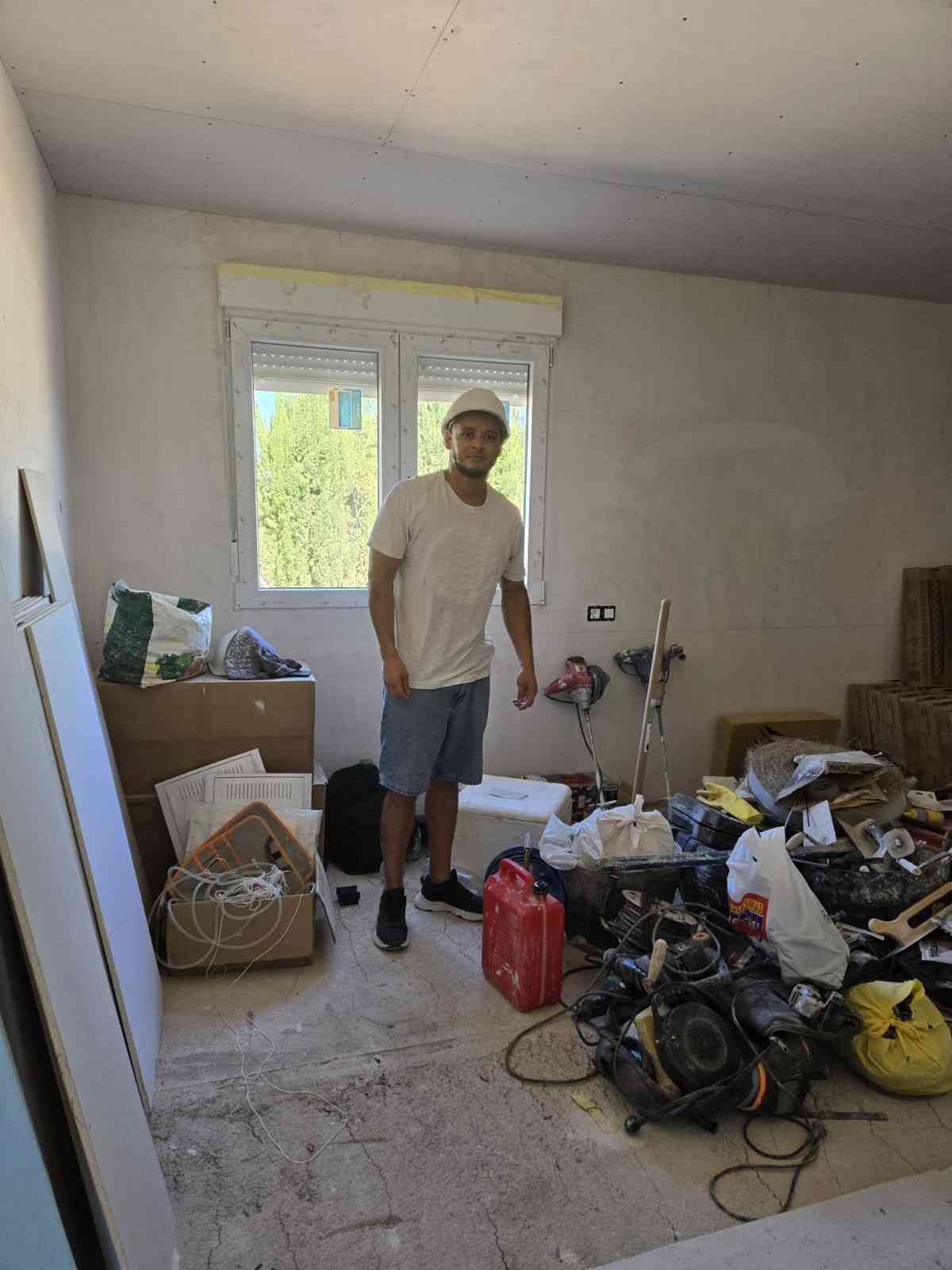 Una persona se encuentra de pie en una habitación desordenada con herramientas, bolsas.