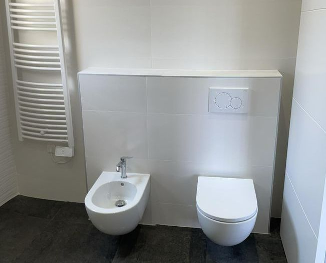 Un bidet, des WC suspendus et un sèche-serviettes installés dans une salle de bains.