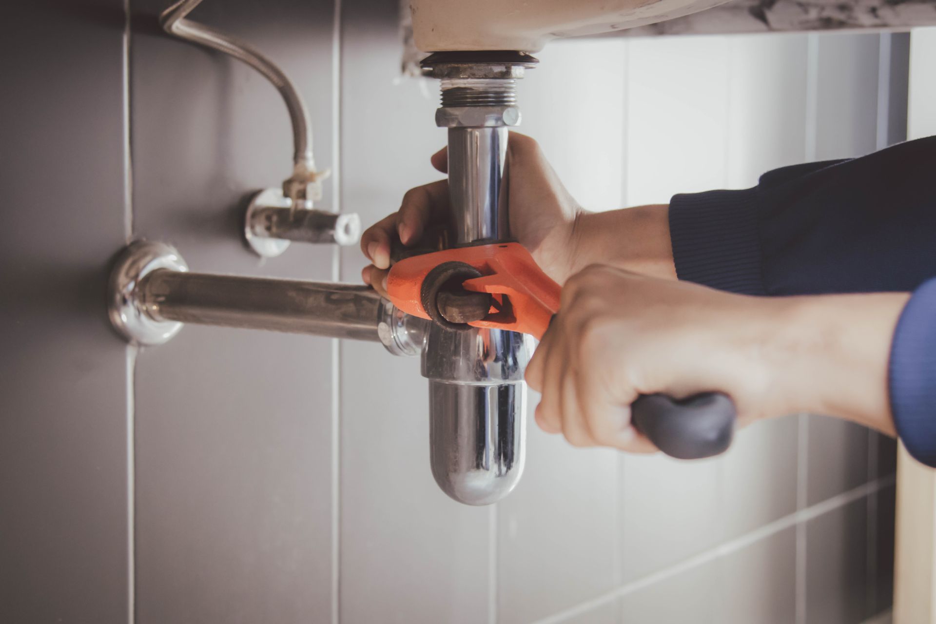 Un gros plan sur les mains d'un professionnel avec une clé plate et un siphon de lavabo.
