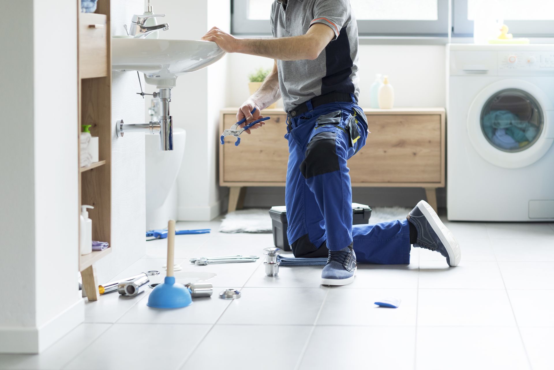 Un plombier devant un lavabo avec des outils posés par terre.