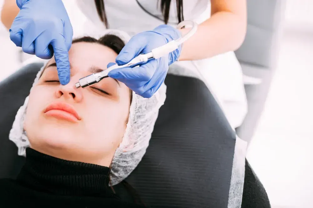 Mujer recibiendo un tratamiento facial; practicante con manos enguantadas utilizando una herramienta en la nariz