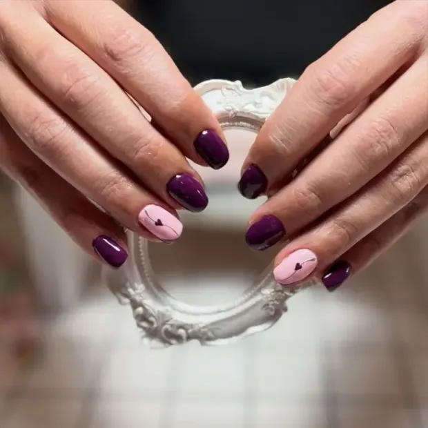 Manos con uñas moradas y rosas, sosteniendo un pequeño espejo blanco decorativo.