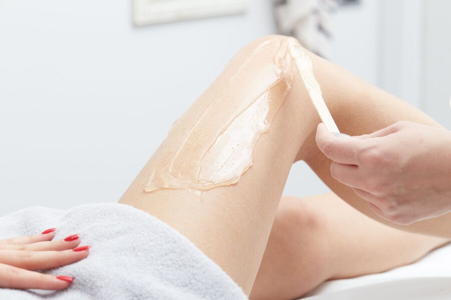 Depilación de piernas con cera caliente aplicada y retirada de la pierna de una persona en un entorno de spa.