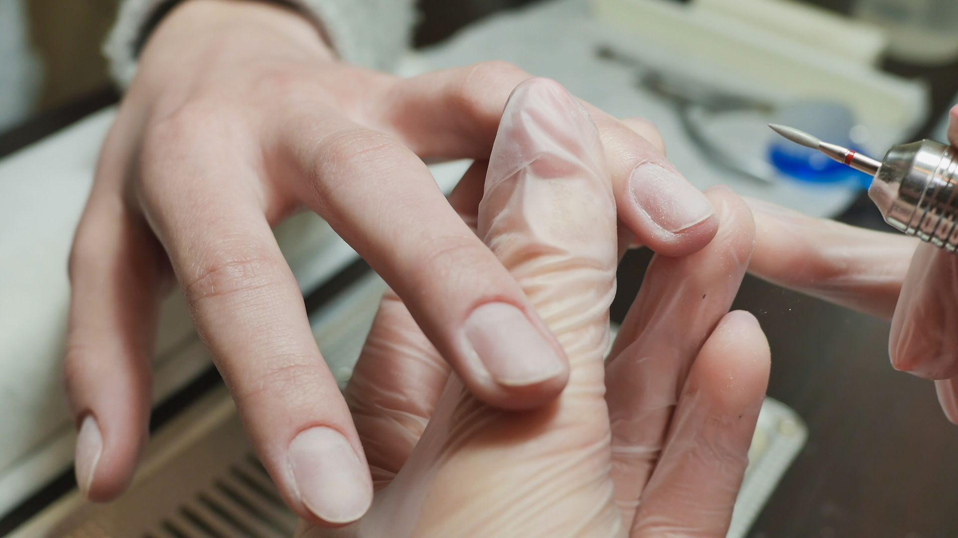 A una persona le están trabajando las uñas de la mano con un taladro de uñas en un salón.