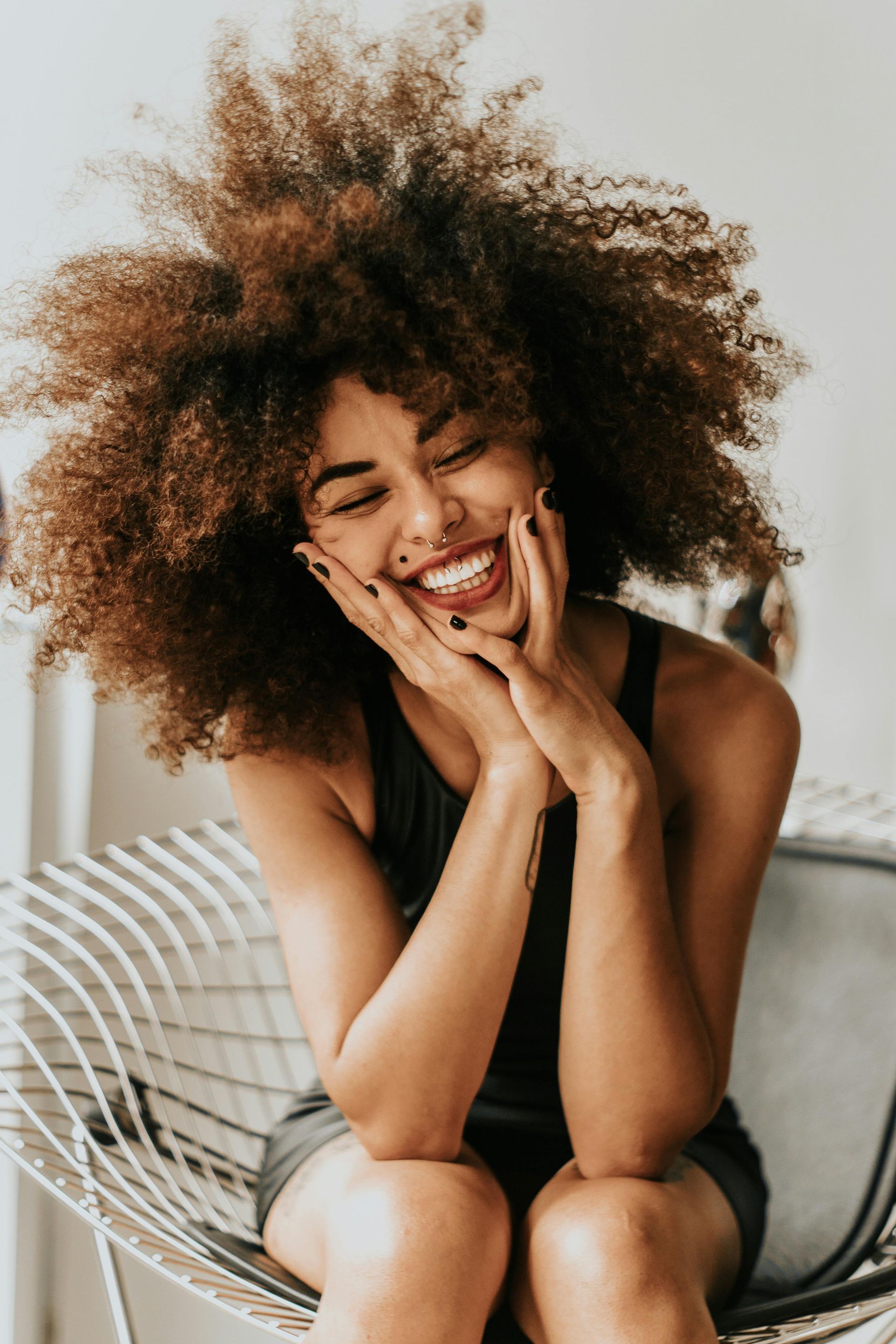 Una mujer con cabello rizado está sentada en una silla y sonriendo.