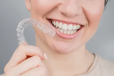 Una mujer sonríe mientras sostiene un aparato transparente en su boca.
