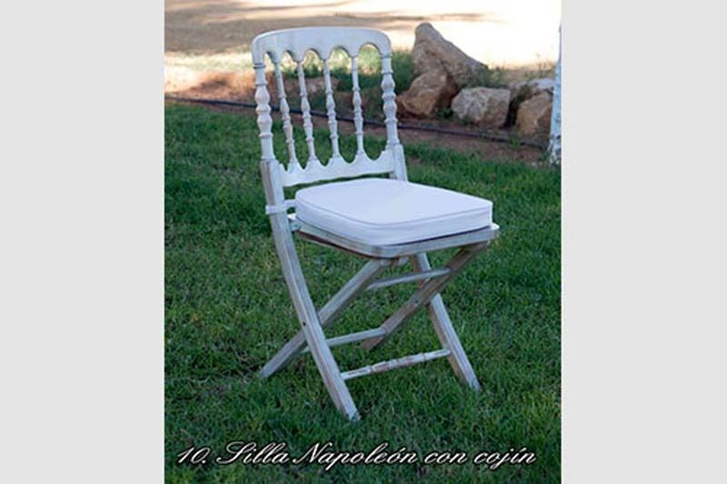 Una silla plegable blanca con un cojín blanco está sentada en el césped.