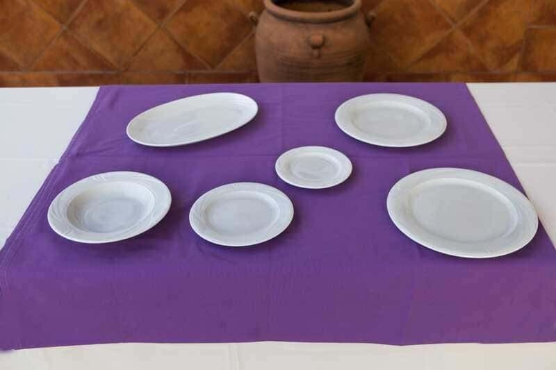 Seis platos blancos están sobre un mantel morado sobre una mesa.
