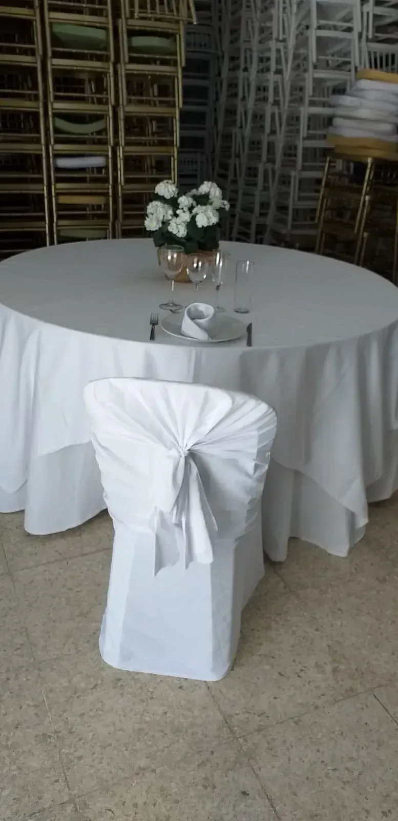 Una mesa redonda con un mantel blanco y sillas blancas.