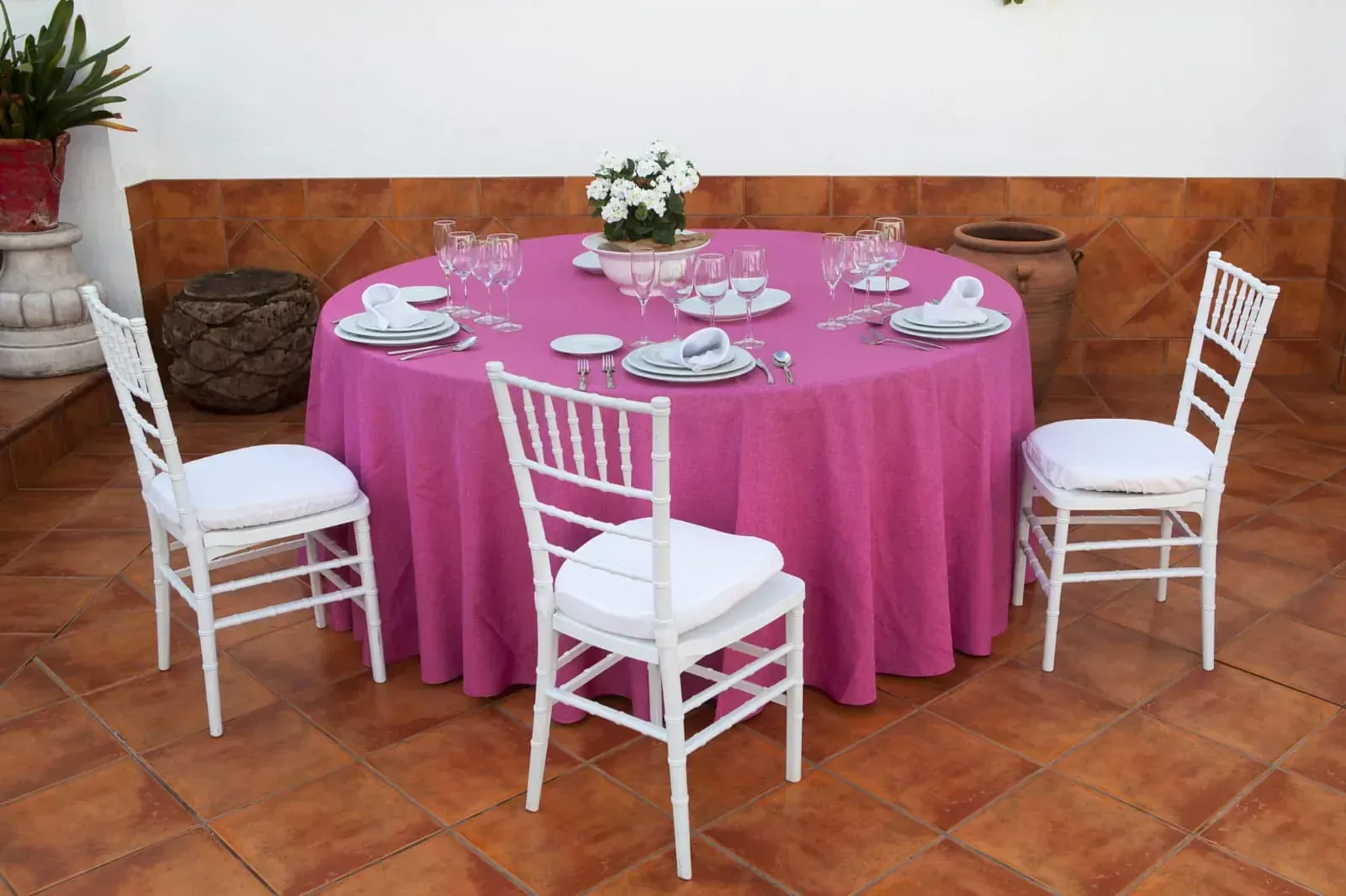 Una mesa con un mantel rosa y sillas blancas.