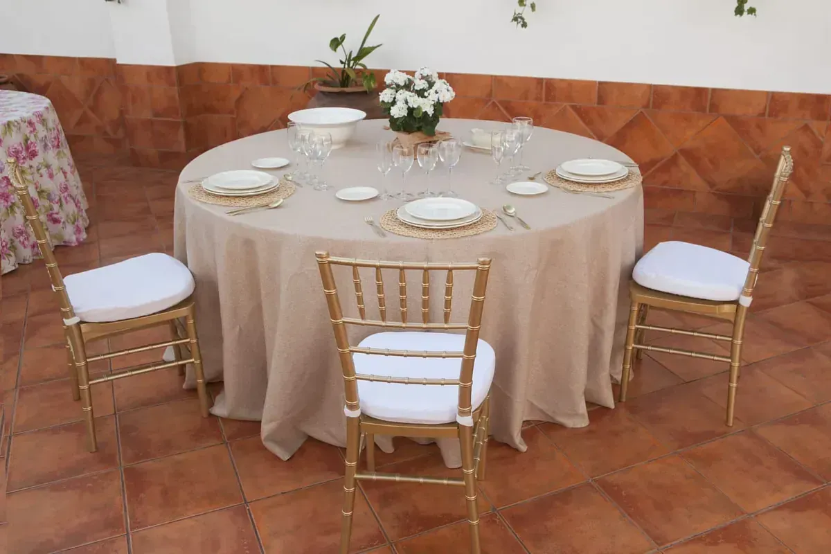 Una mesa redonda con mantel y sillas sobre un suelo de baldosas.