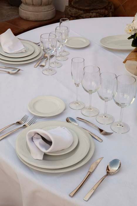 Una mesa puesta con platos blancos y cubiertos y copas de vino.