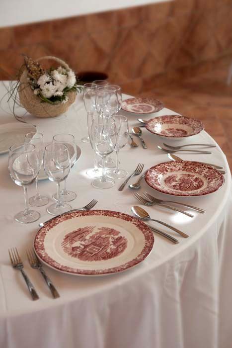 Una mesa está puesta con platos, vasos, cubiertos y una cesta de flores.