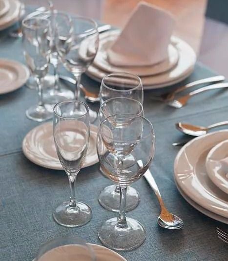 Una mesa puesta con platos, copas de vino, cubiertos y servilletas.