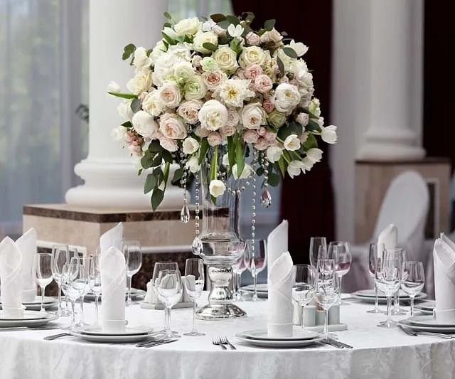 Una mesa preparada para una recepción de boda con un jarrón de flores encima.