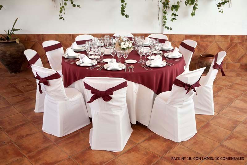 Una mesa con un mantel rojo y sillas blancas.