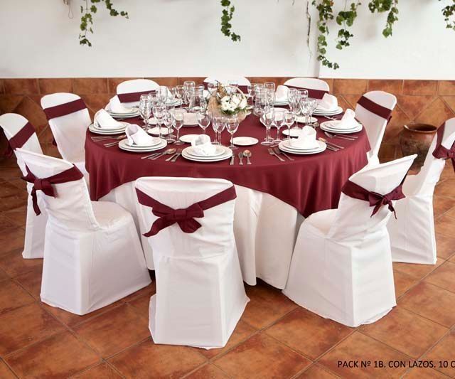 Una mesa redonda con un mantel granate y sillas blancas.