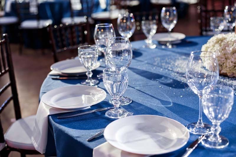 Una mesa preparada para una recepción de boda con platos, copas de vino y cubiertos.