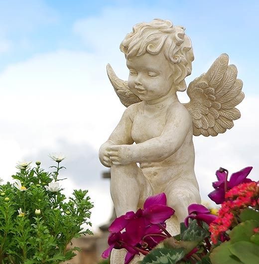 Una estatua de un querubín sentado en un macizo de flores