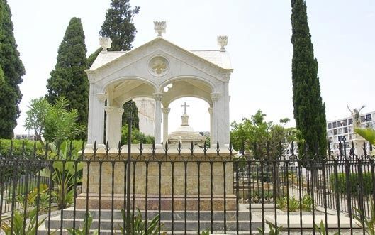 Un pequeño edificio blanco con una cruz en la parte superior está detrás de una valla en un cementerio.