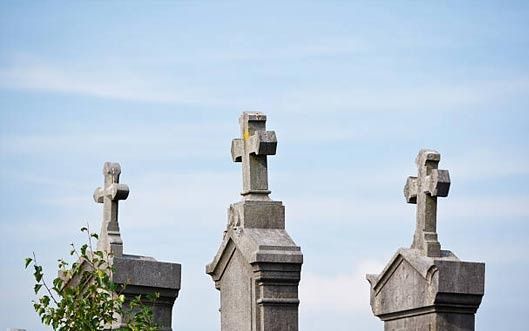 Tres lápidas con cruces encima en un cementerio con un cielo azul de fondo.