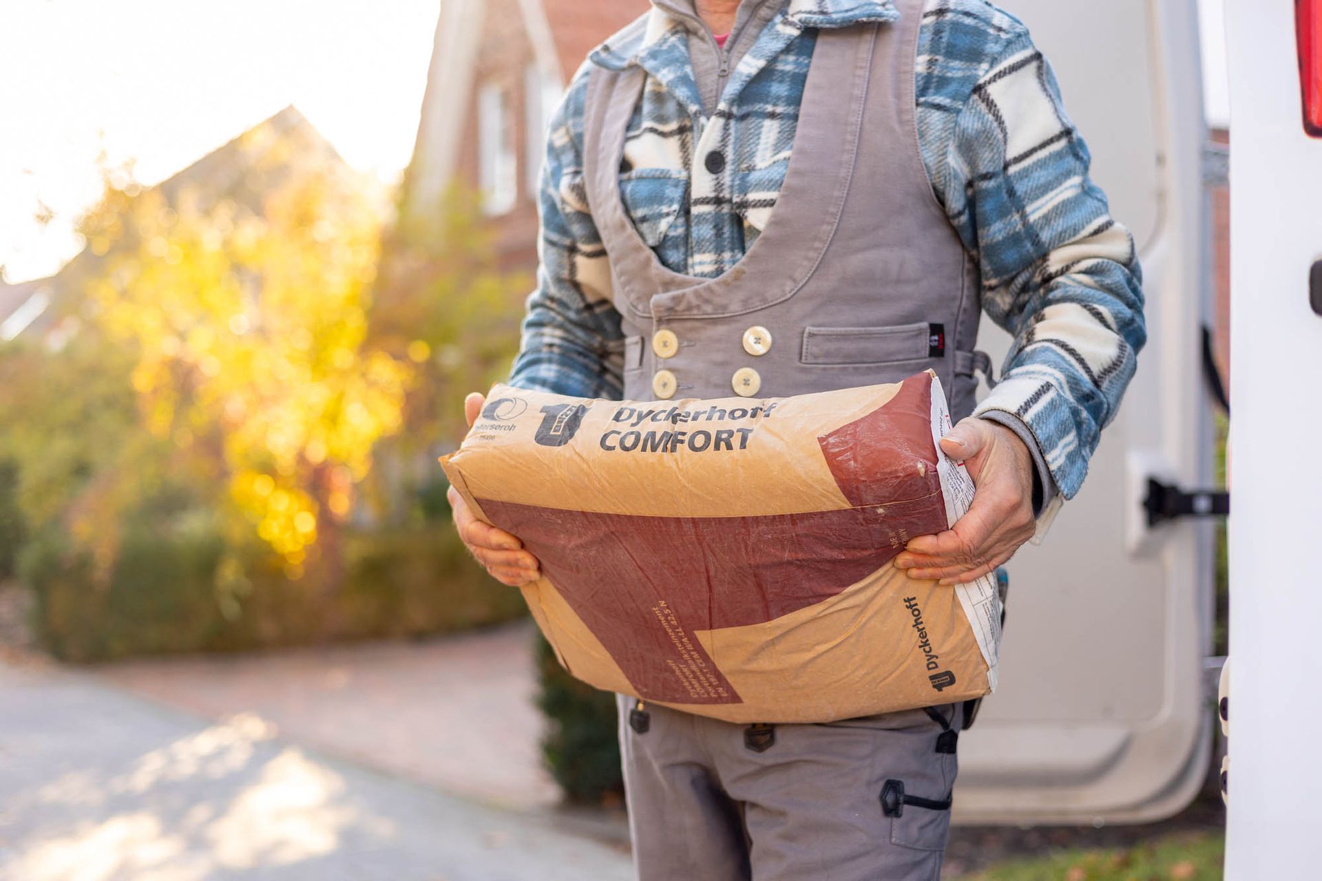 Ein Mann trägt einen Sack Zement vor einem Lieferwagen.