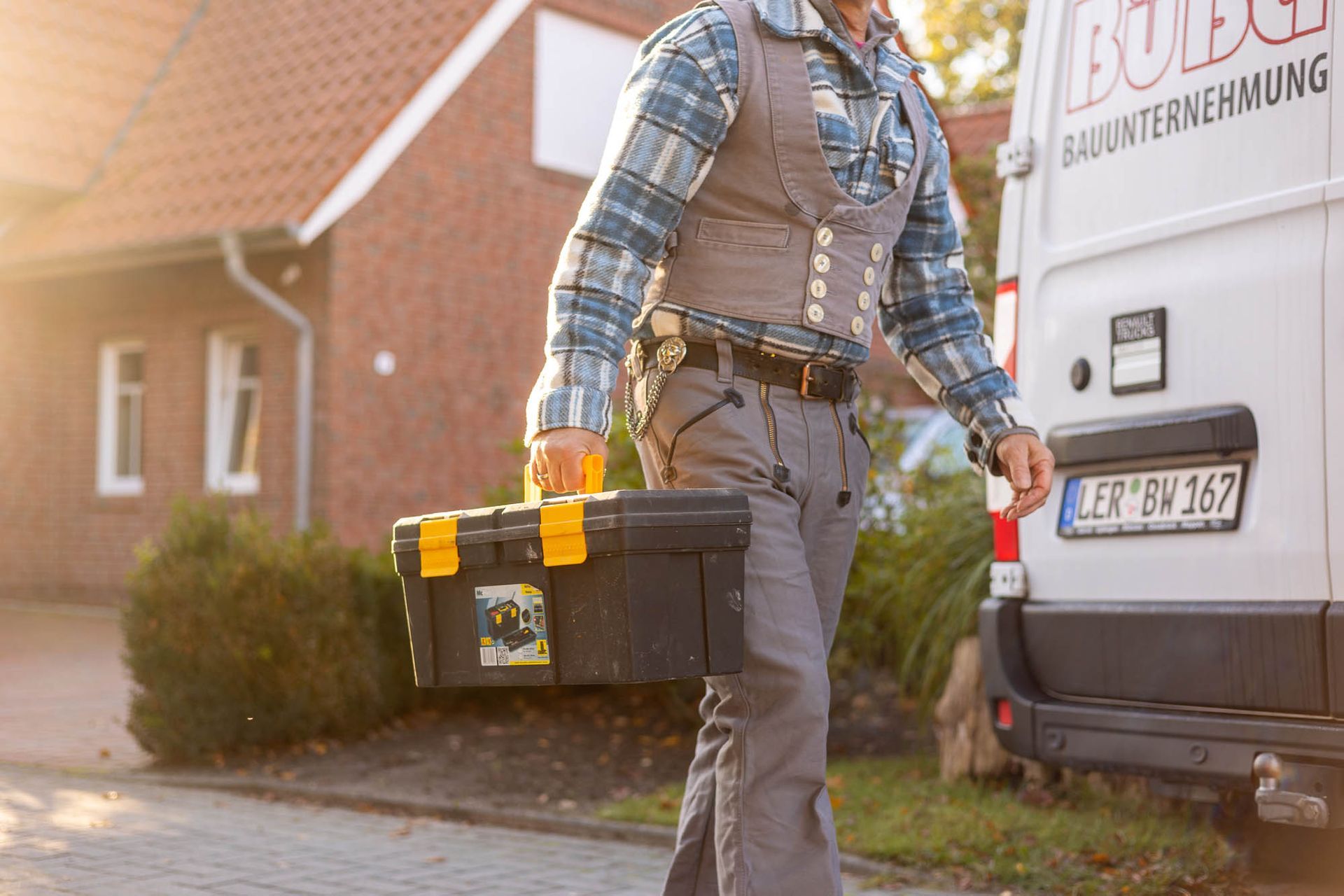 Ein Mann trägt einen Werkzeugkasten vor einem Lieferwagen.