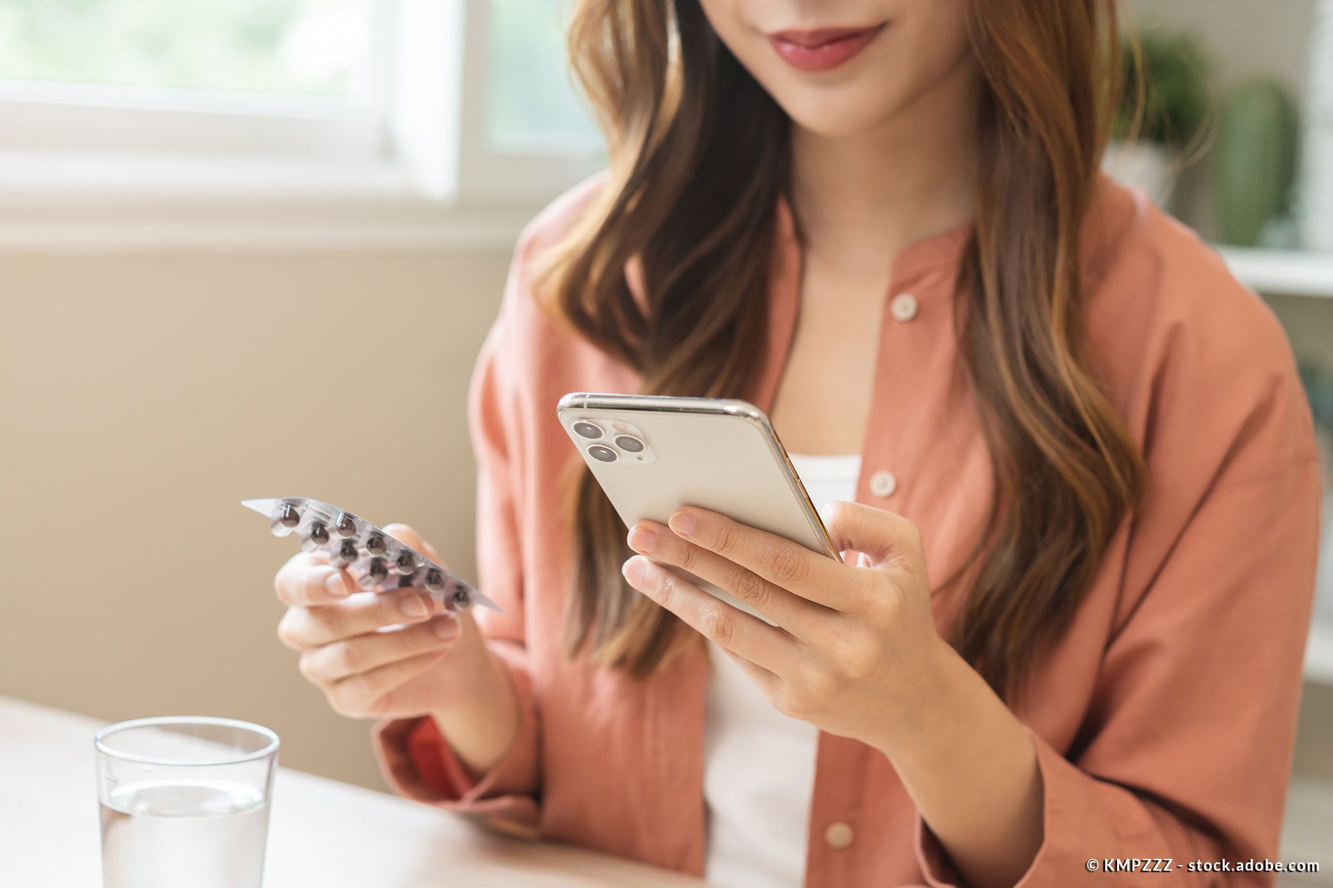 Eine junge Frau hält ein Handy und eine Blisterverpackung in ihren Händen
