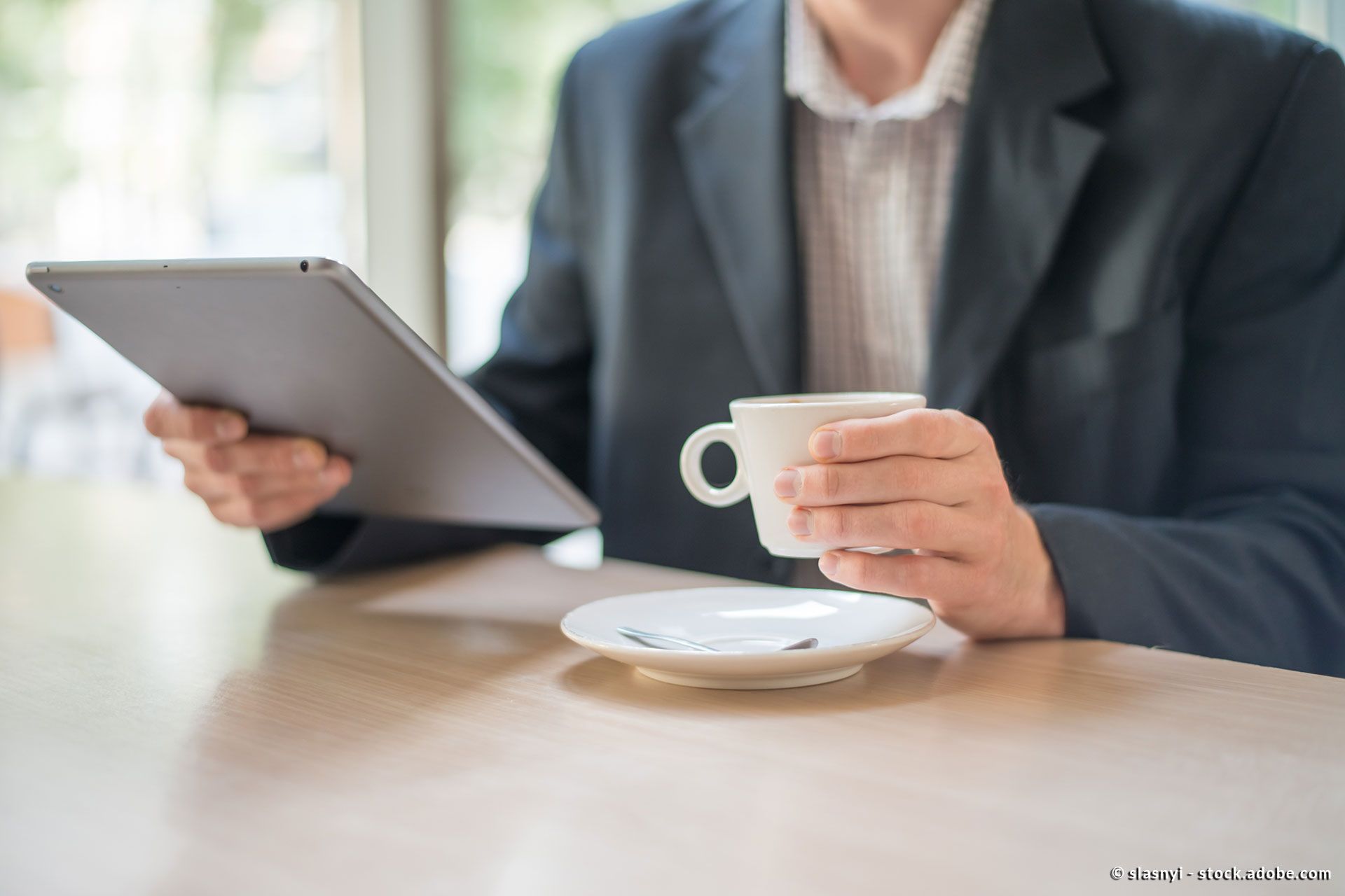 Ein Mann liest News auf seinem Tablet und trinkt dabei eine Tasse Kaffee