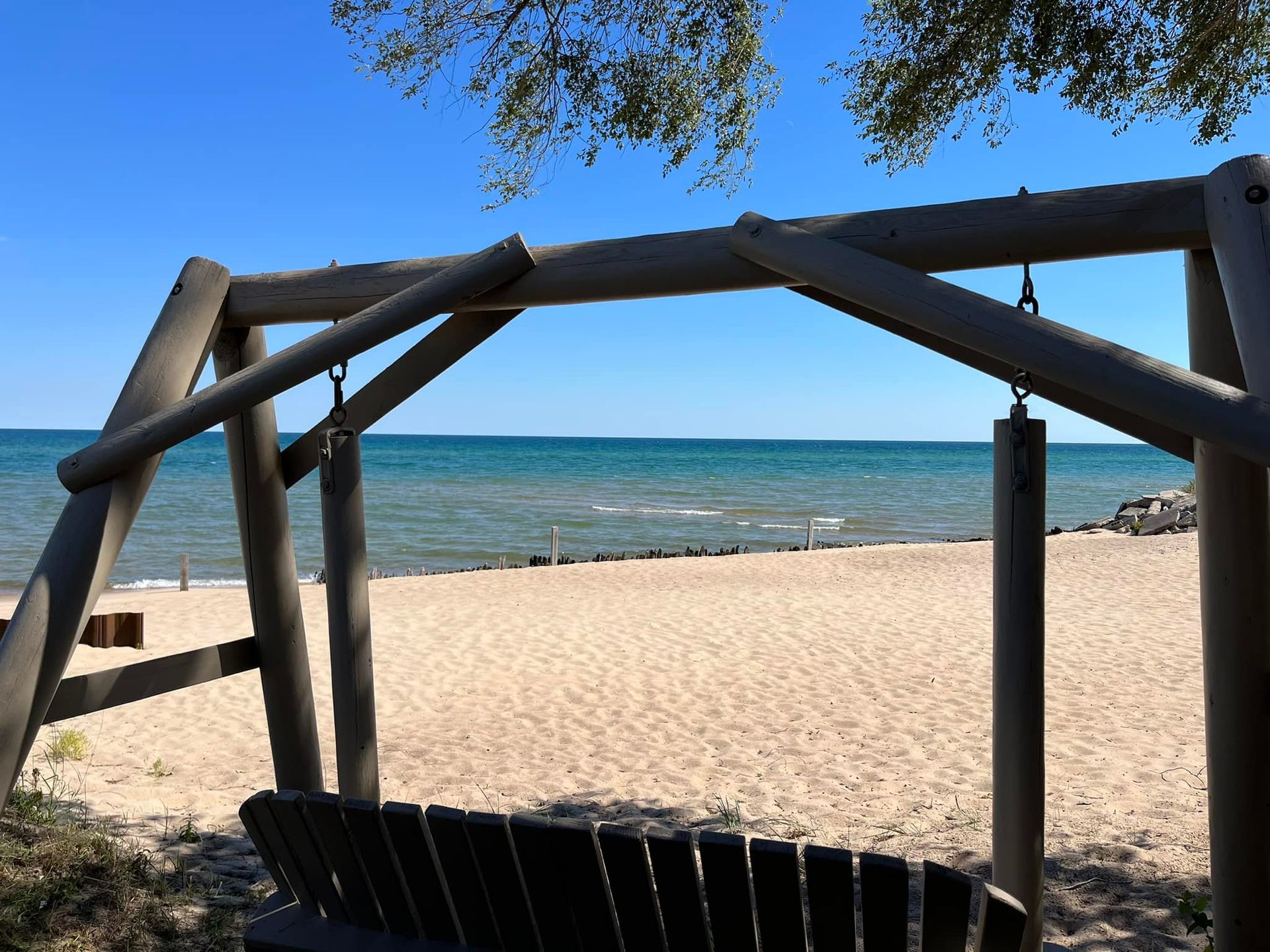 A wooden porch swing overlooks a sandy beach and a bright blue ocean under a clear sky.