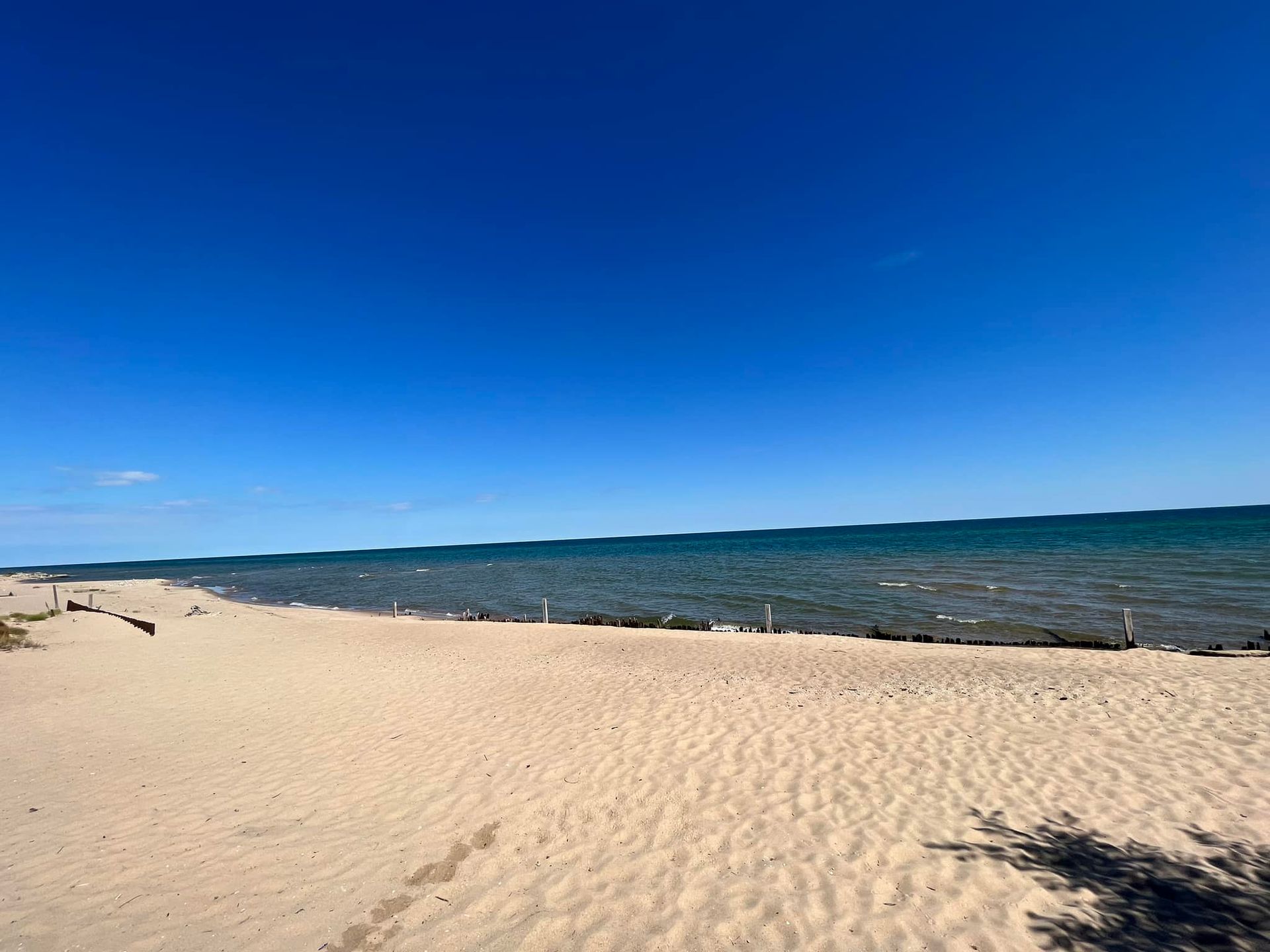 A wide, sandy beach meets a calm, blue ocean under a clear, bright sky.