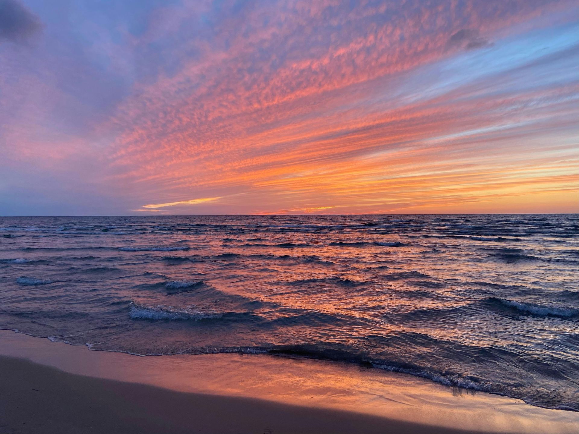 Vibrant sunset over a calm sea, with pink and orange light reflecting on the water and sandy beach.