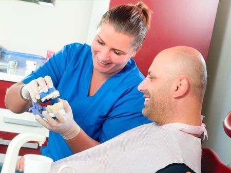 Una dentista le muestra a un hombre un modelo de sus dientes.