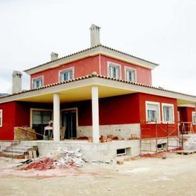 Una casa de dos plantas con paredes rojas y molduras blancas, que cuenta con un porche cubierto y materiales de construcción en el suelo.