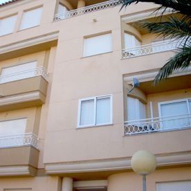 Un edificio de apartamentos de varias plantas de color beige con balcones, contraventanas blancas cerradas y una farola esférica en primer plano.
