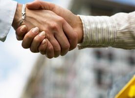 Dos personas dándose la mano, con una obra en construcción o un sitio de construcción borroso al aire libre al fondo.